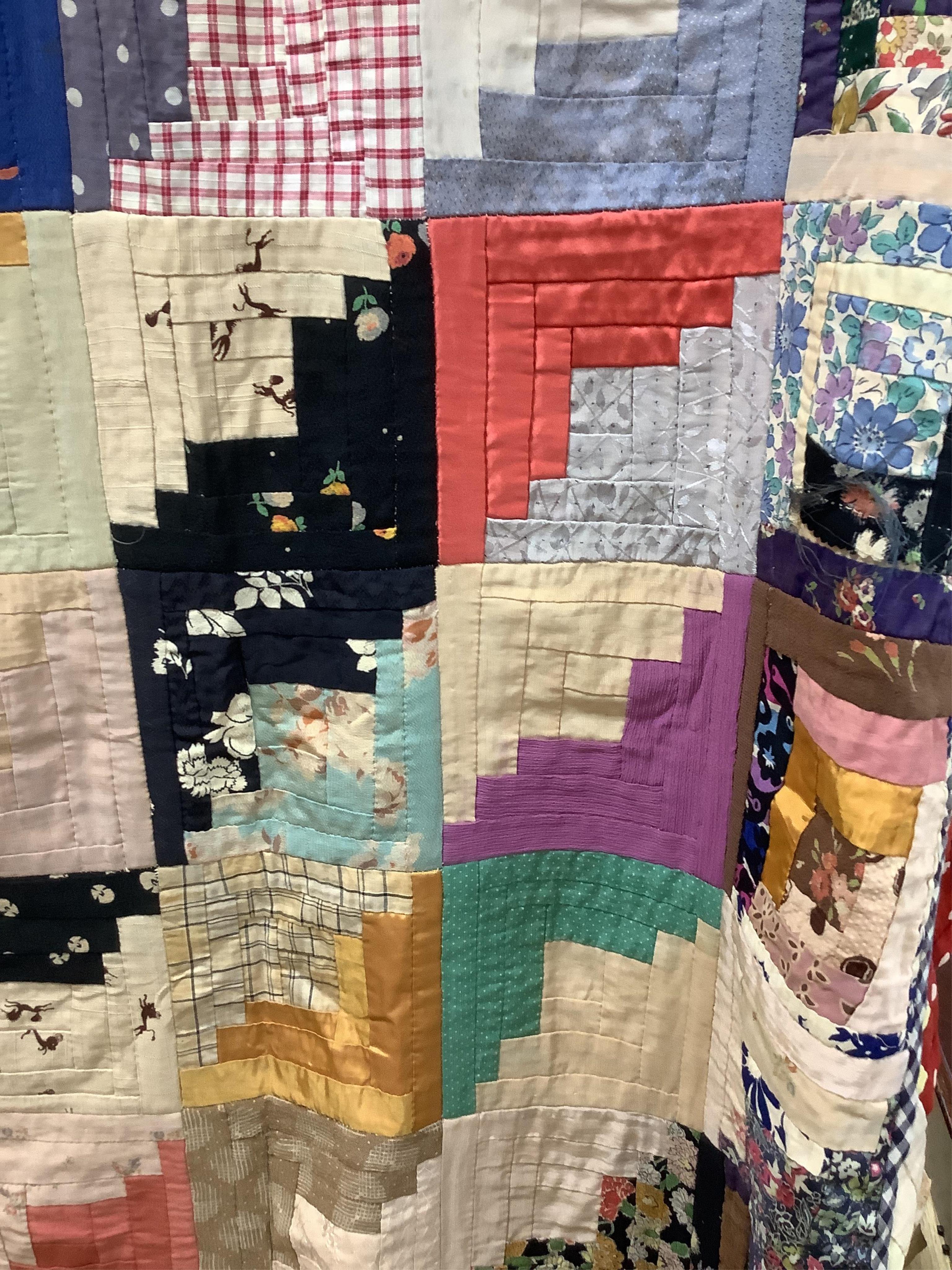 An early 20th century Log Cabin patchwork bedcover, worked in plain and printed silk, rayons and cottons from 1900 to 1940’s. Edged with a triangular patchwork border on three sides. Cover unlined. 158cm wide x 192cm lon